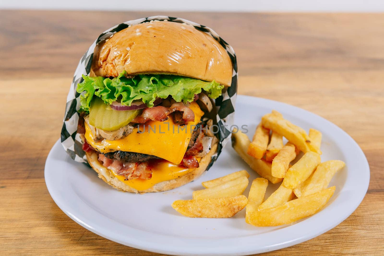 Delicious homemade hamburger on a plate on a wooden table. Big cheeseburger with french fries served on wooden table