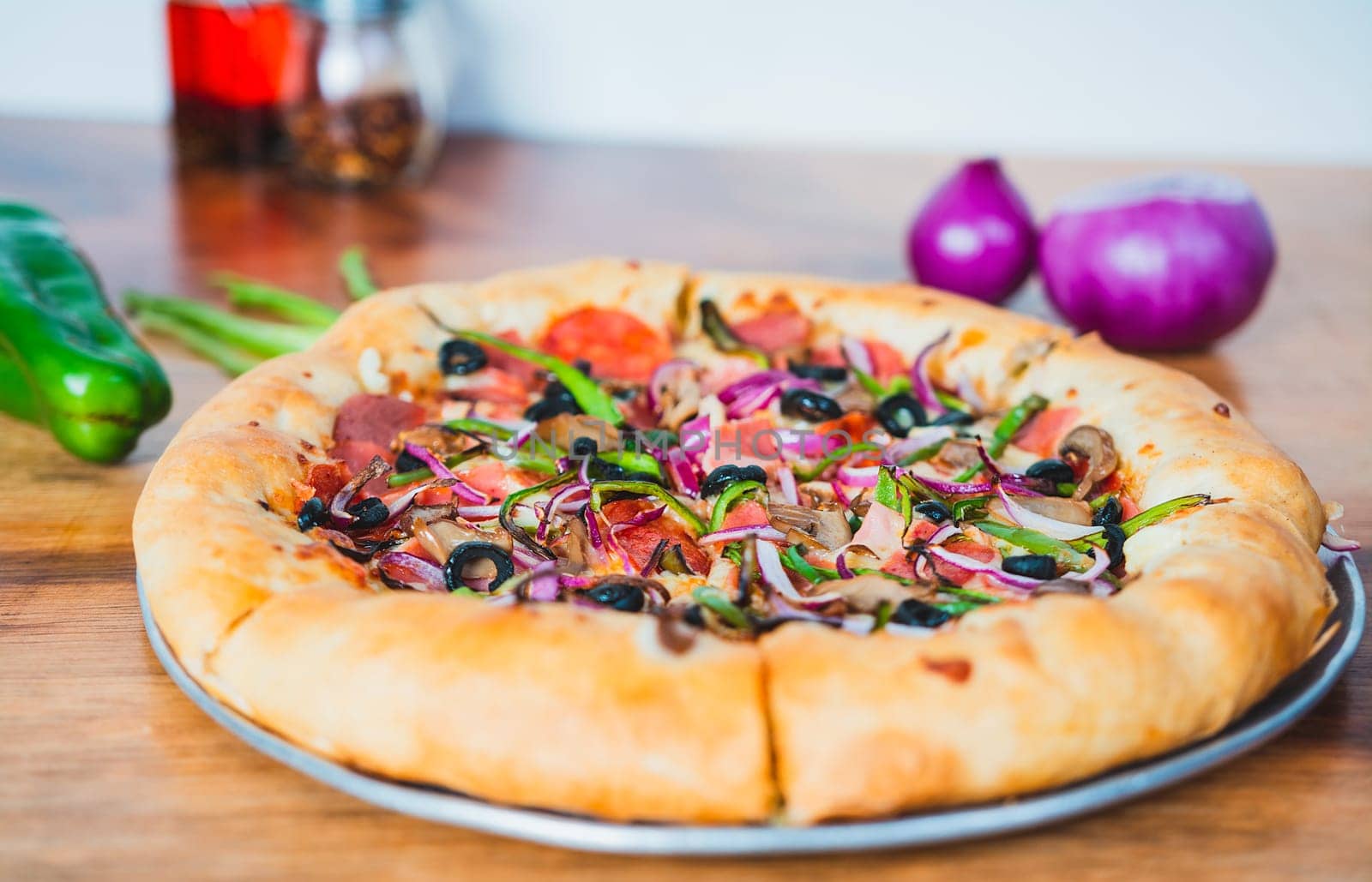 Close up of supreme pizza with olives and vegetables on wooden table. Delicious supreme pizza with vegetables served on table by isaiphoto