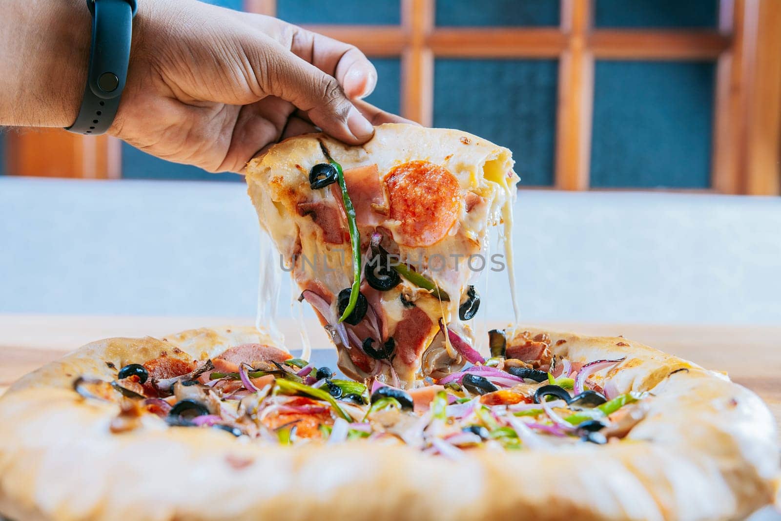 Hand taking a delicious slice of supreme pizza with vegetables. Hand taking a slice of supreme pizza on wooden table by isaiphoto