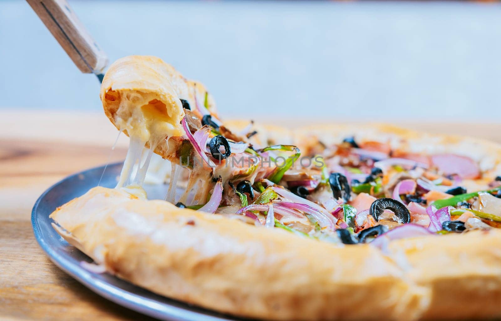 Close-up spatula taking a slice of supreme pizza with vegetables. Hand taking a slice of supreme pizza with spatula