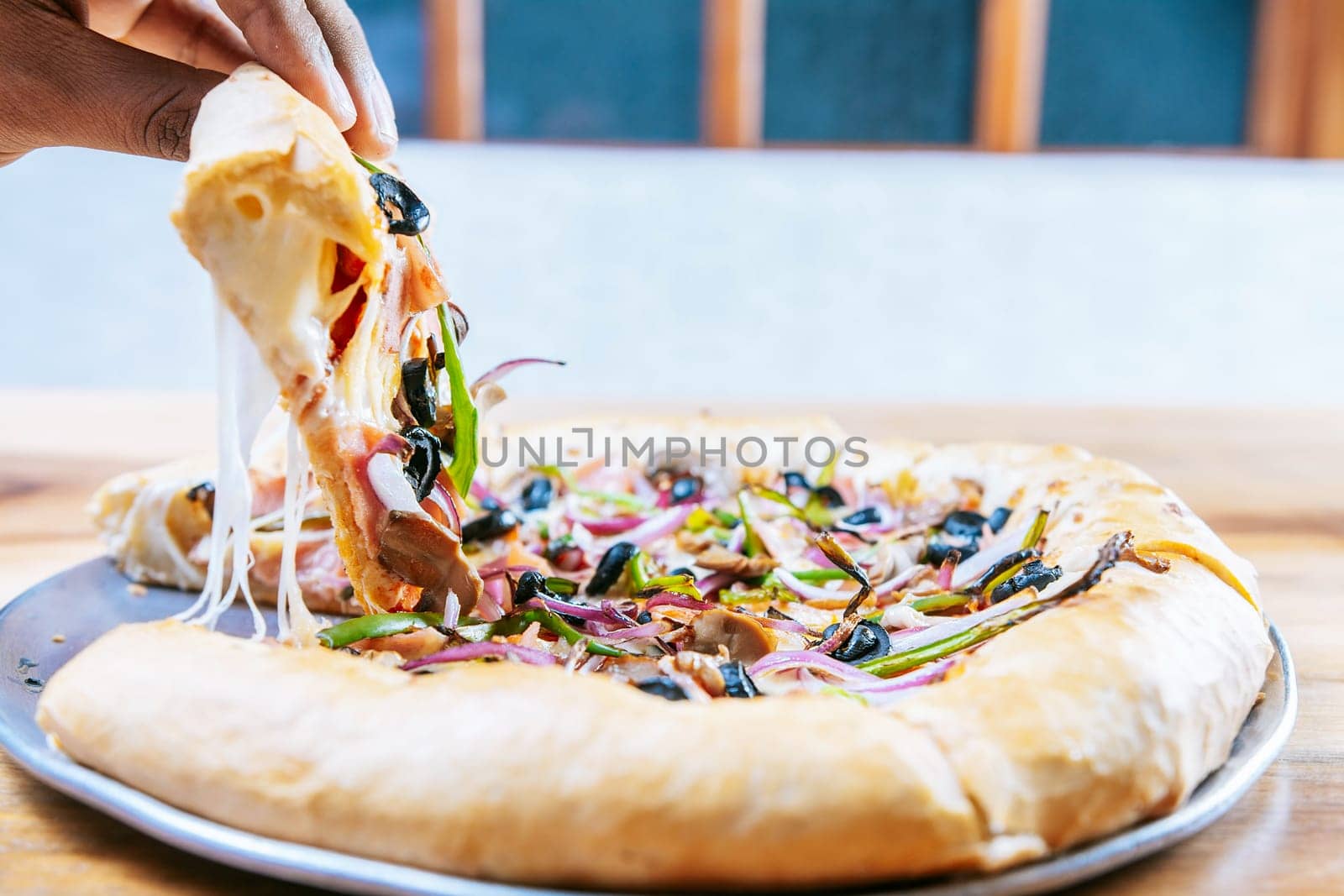 Hand taking a slice of supreme pizza on wooden table. Close-up of a hand taking a delicious slice of supreme pizza with vegetables by isaiphoto