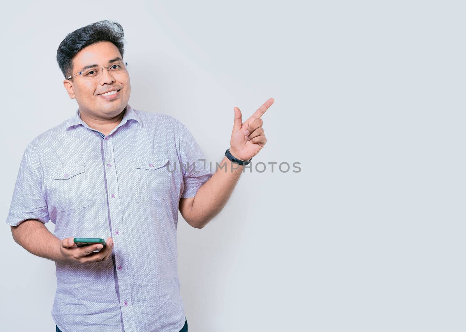 Young latin man holding cellphone pointing to side isolated. Happy guy holding cellphone pointing to the side isolated