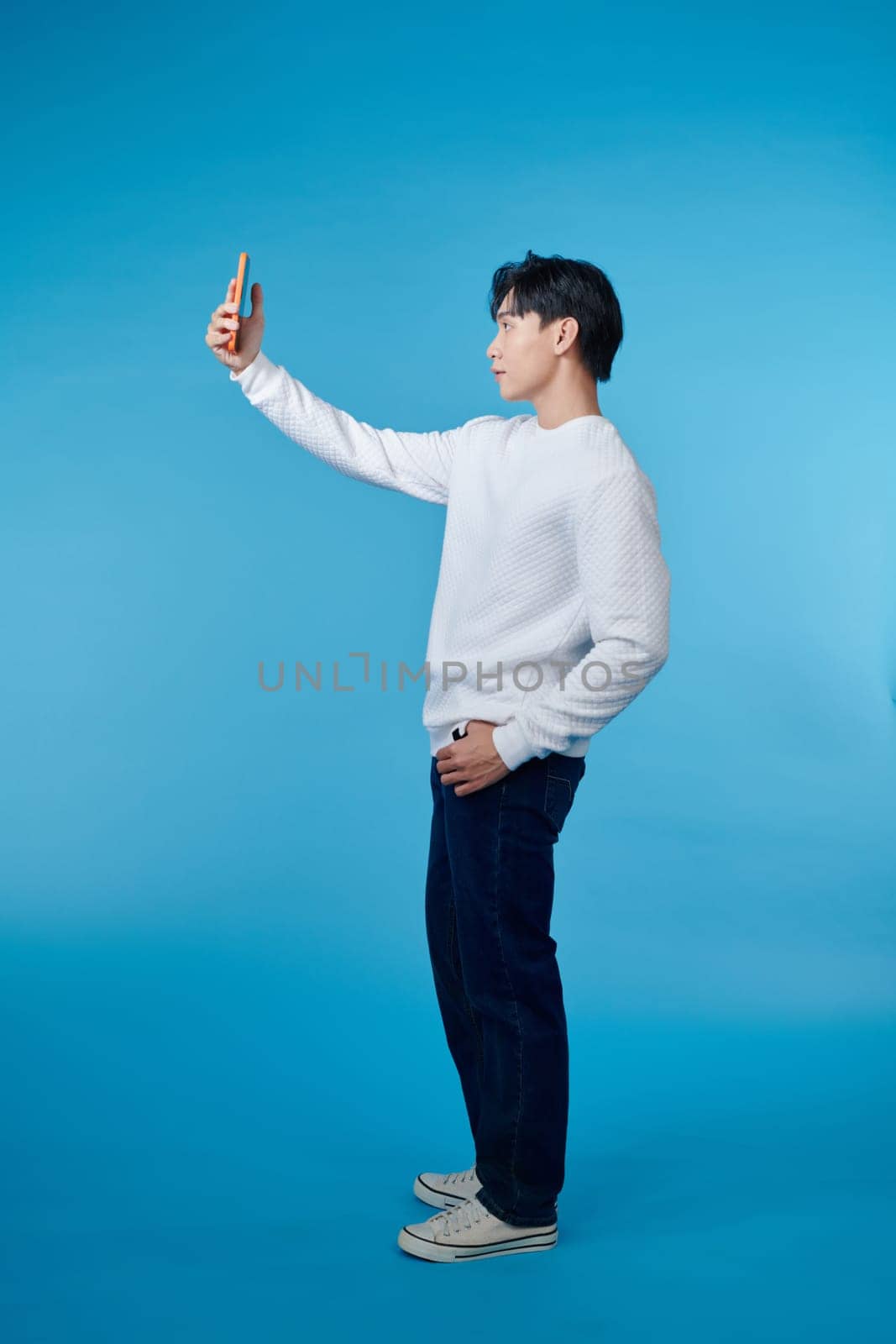 full body young man doing selfie shot on mobile cell phone isolated on blue background by makidotvn