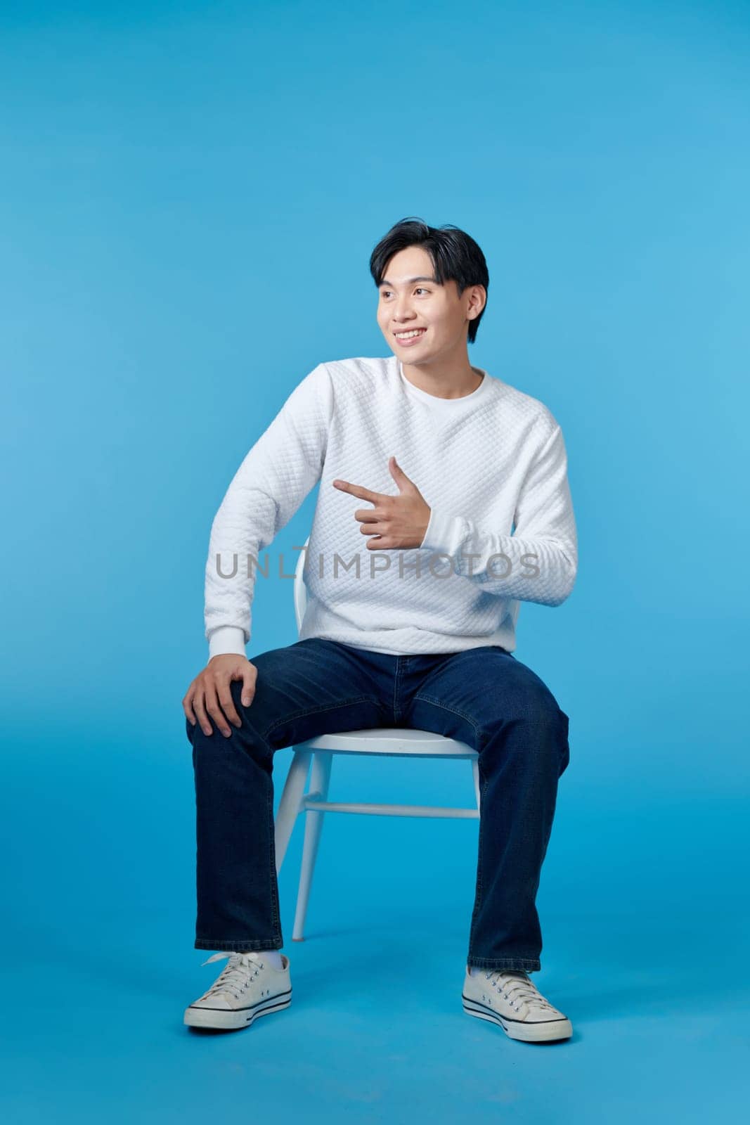 Happy cheerful handsome man pointing finger away while sitting on the chair 