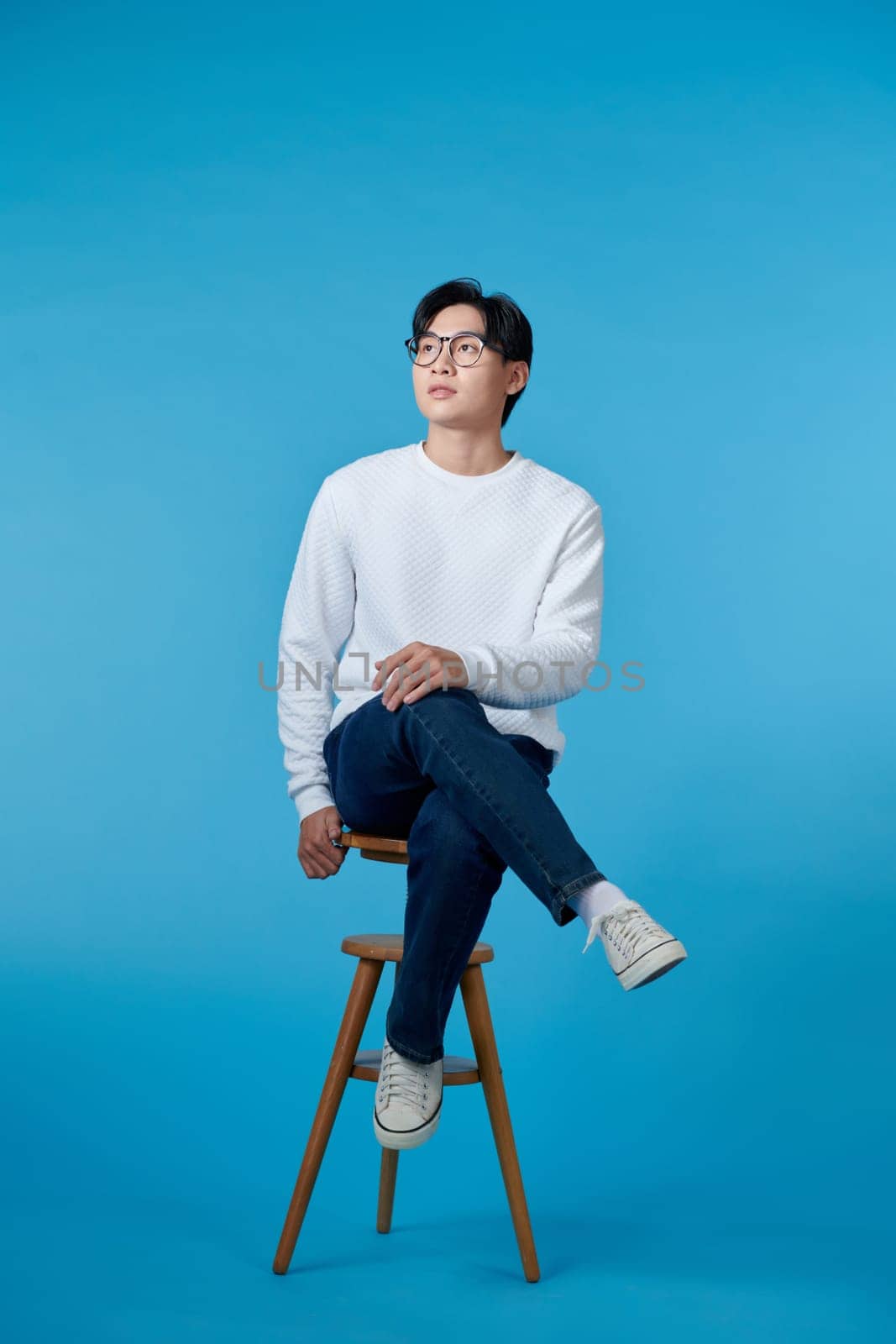 Beautiful asian successful man sitting at white chair and posing to the camera. Copy space. by makidotvn
