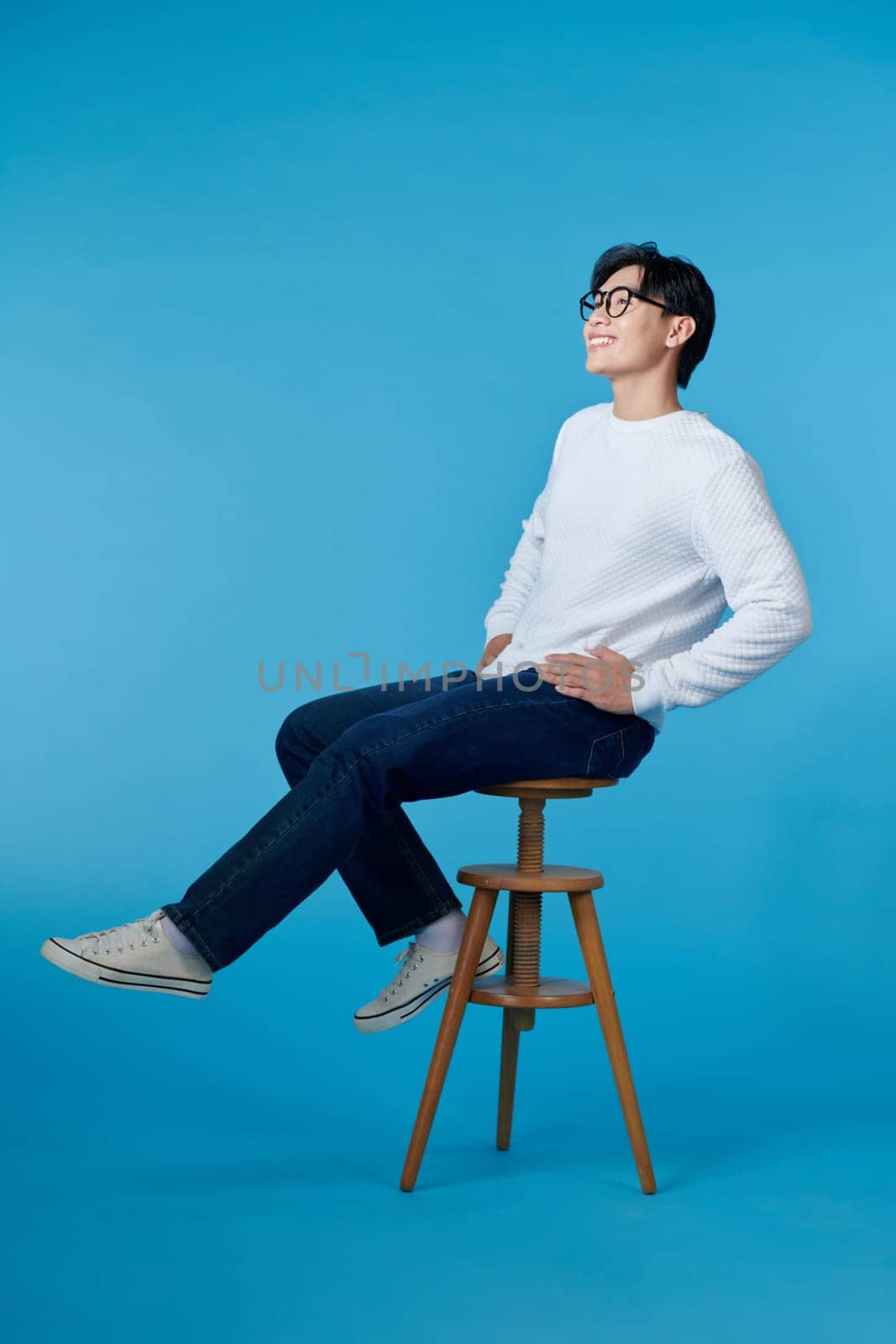 man sitting on a chair look side on blue background by makidotvn
