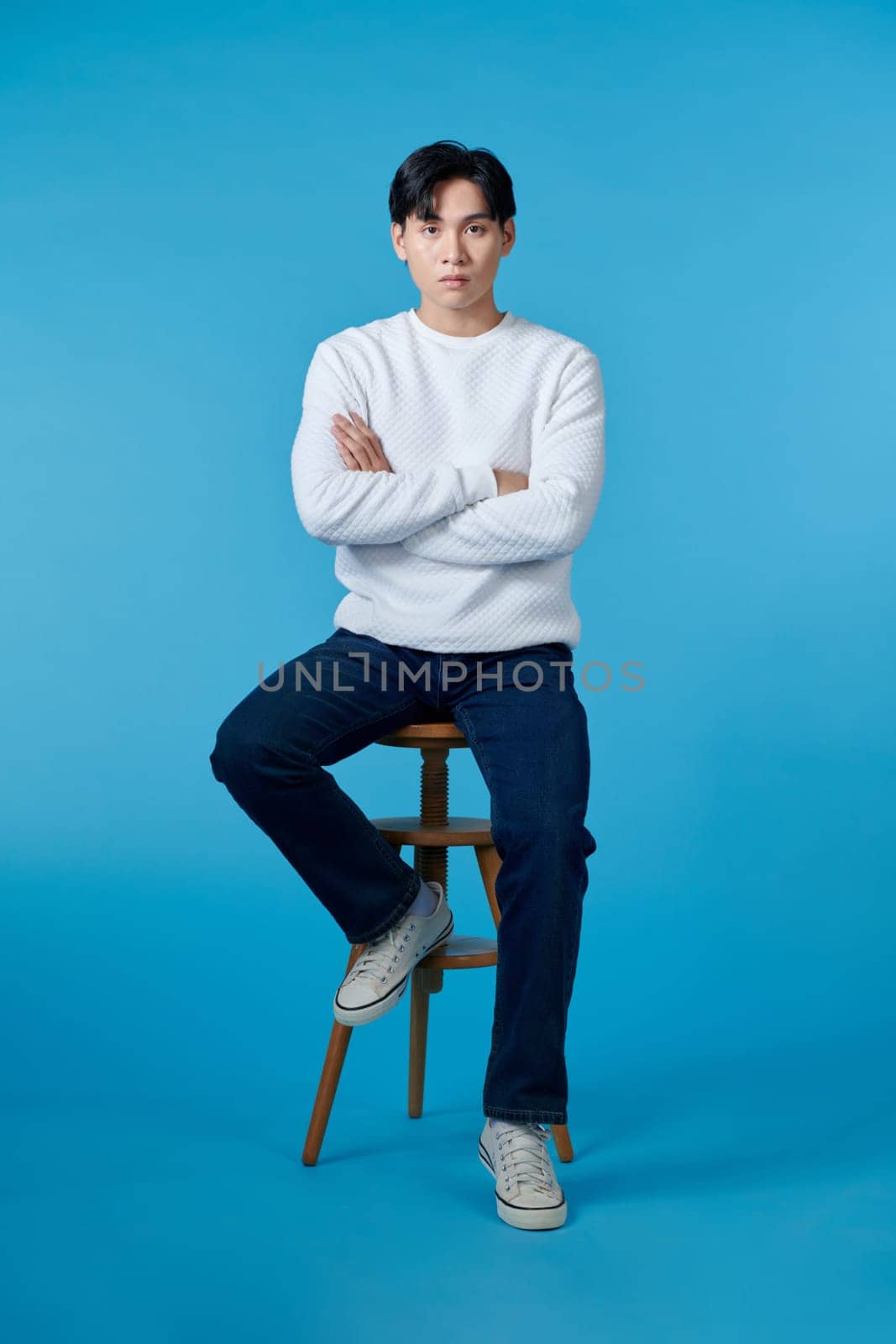 handsome young man sitting on the chair, isolated on blue background by makidotvn