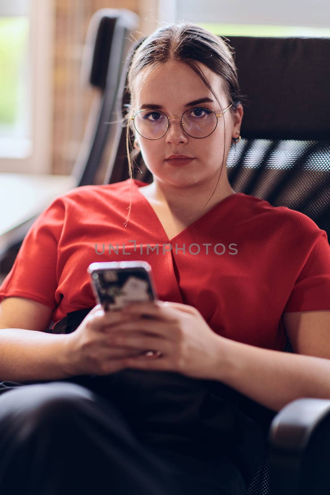 A businesswoman resting on a short break from work in a modern startup coworking center, using her smartphone to unwind and recharge