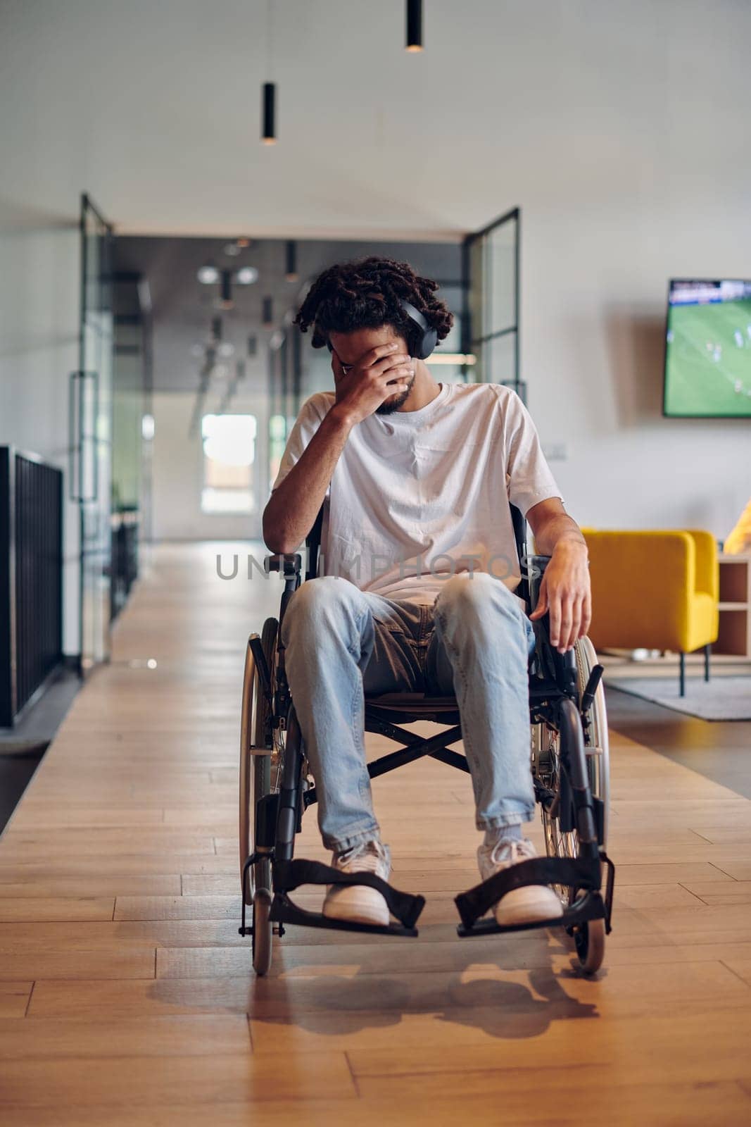 A sad businessman in a wheelchair occupies a hallway within a modern startup coworking center, embodying inclusivity and determination in the business environment.