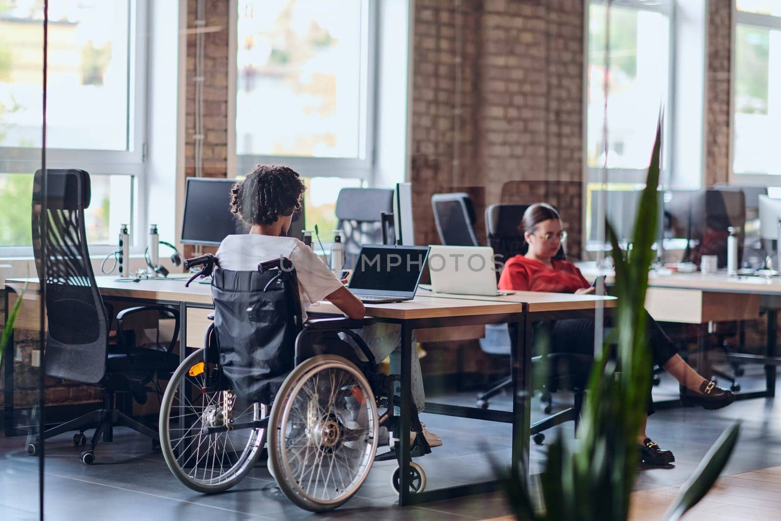 Business colleagues work within a modern startup coworking office, with one of them, an African America in a wheelchair, actively engaging with computers and laptops to collaboratively address various business challenges