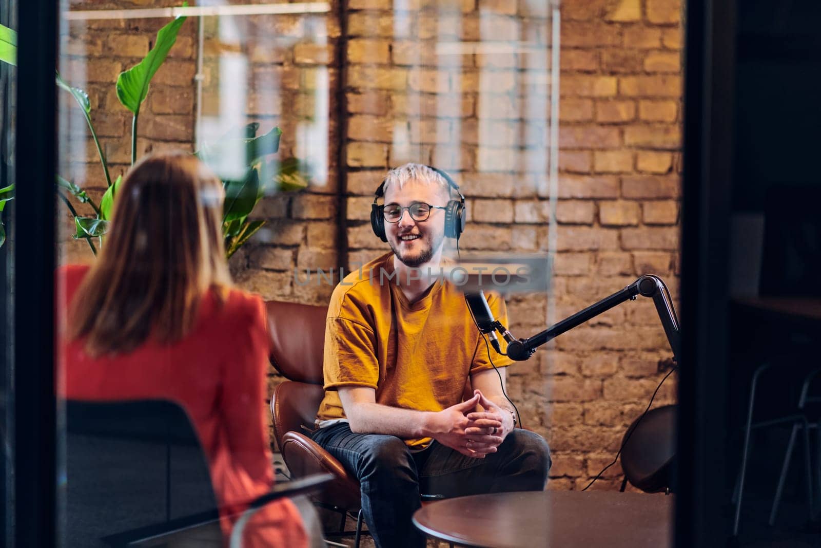 A gathering of young business professionals, some seated in a glass-walled office, engage in a lively conversation and record an online podcast, embodying modern collaboration and dynamic interaction by dotshock