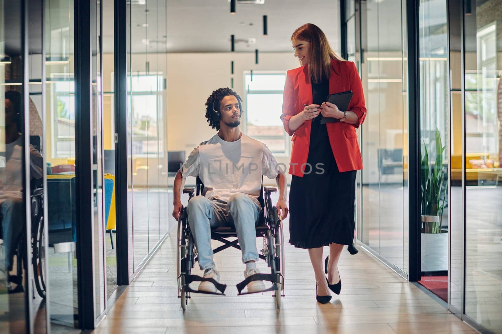 A group of young business people in a modern glass-walled office captures the essence of diversity and collaboration, while two colleagues, including an African American businessman in a wheelchair, reflect inclusivity and discuss solving business problems by dotshock