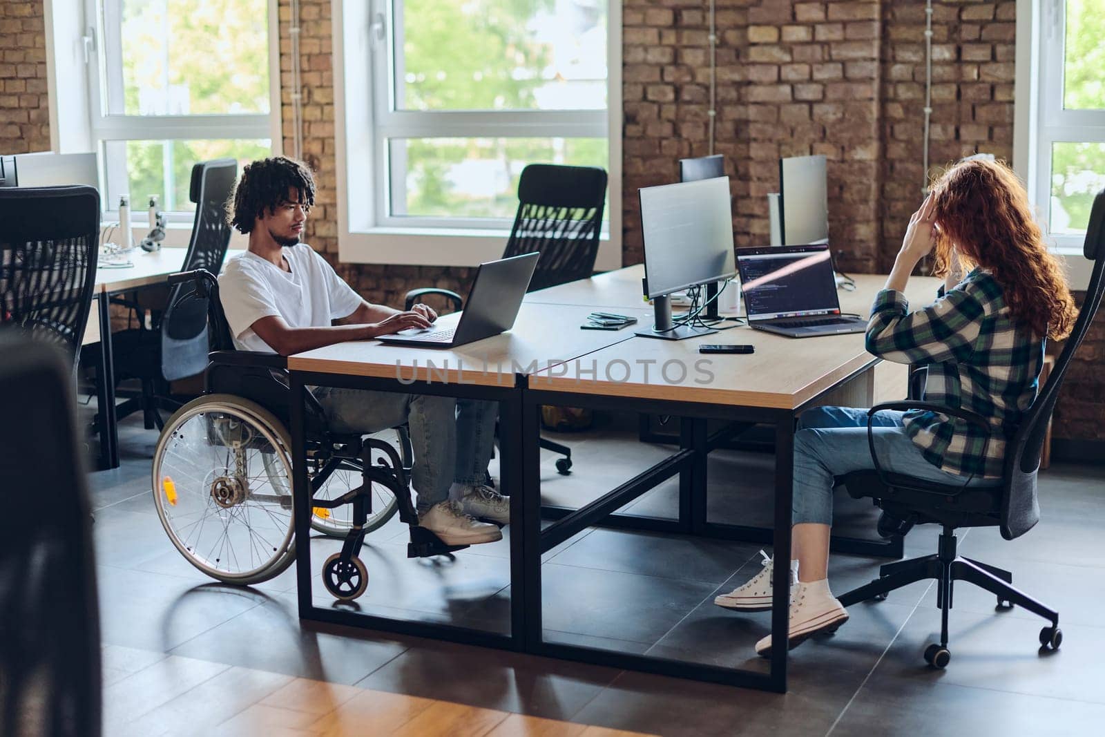 Business colleagues work within a modern startup coworking office, with one of them, an African America in a wheelchair, actively engaging with computers and laptops to collaboratively address various business challenges