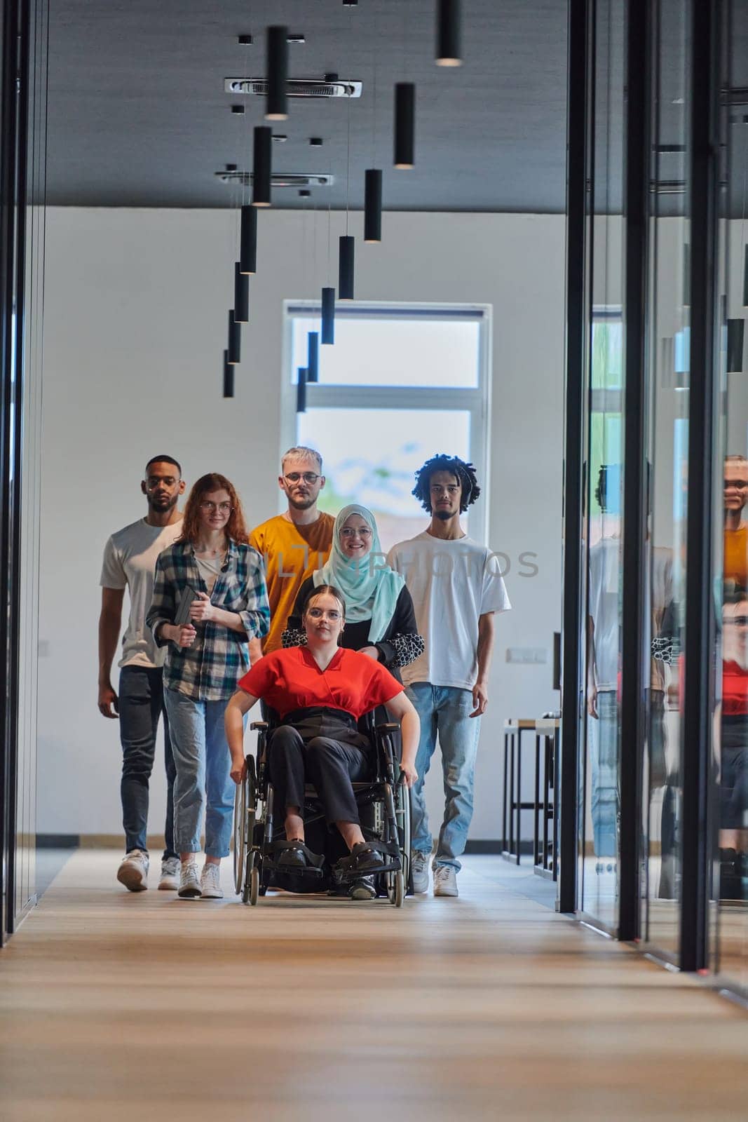 A diverse group of young business people walking a corridor in the glass-enclosed office of a modern startup, including a person in a wheelchair and a woman wearing a hijab, showing a dynamic mix of innovation and unity. by dotshock