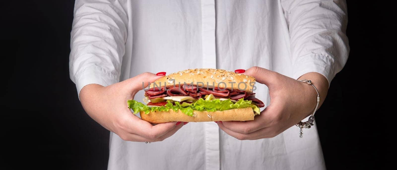 sandwich in women's hands on a black background.