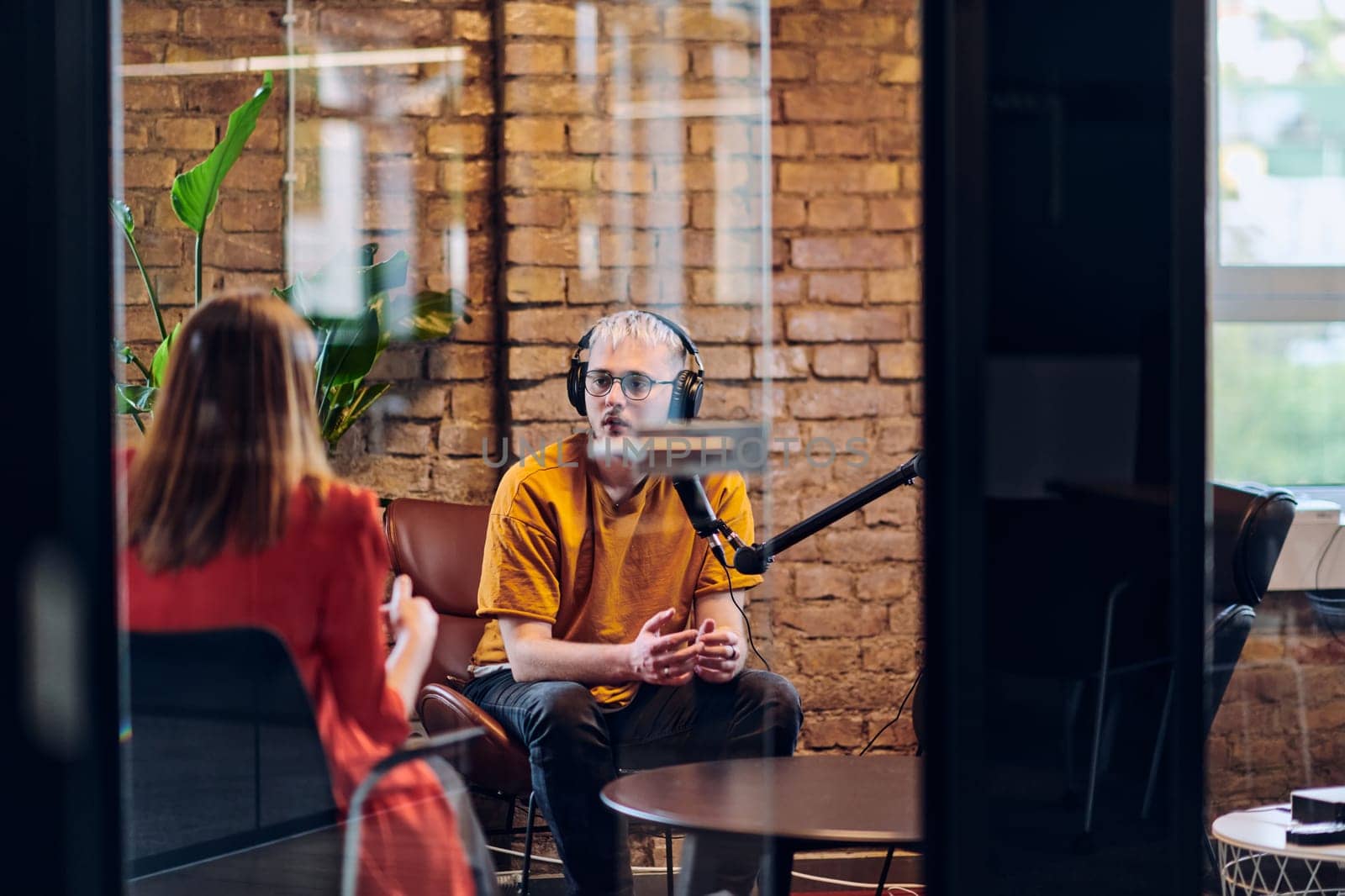 A gathering of young business professionals, some seated in a glass-walled office, engage in a lively conversation and record an online podcast, embodying modern collaboration and dynamic interaction by dotshock