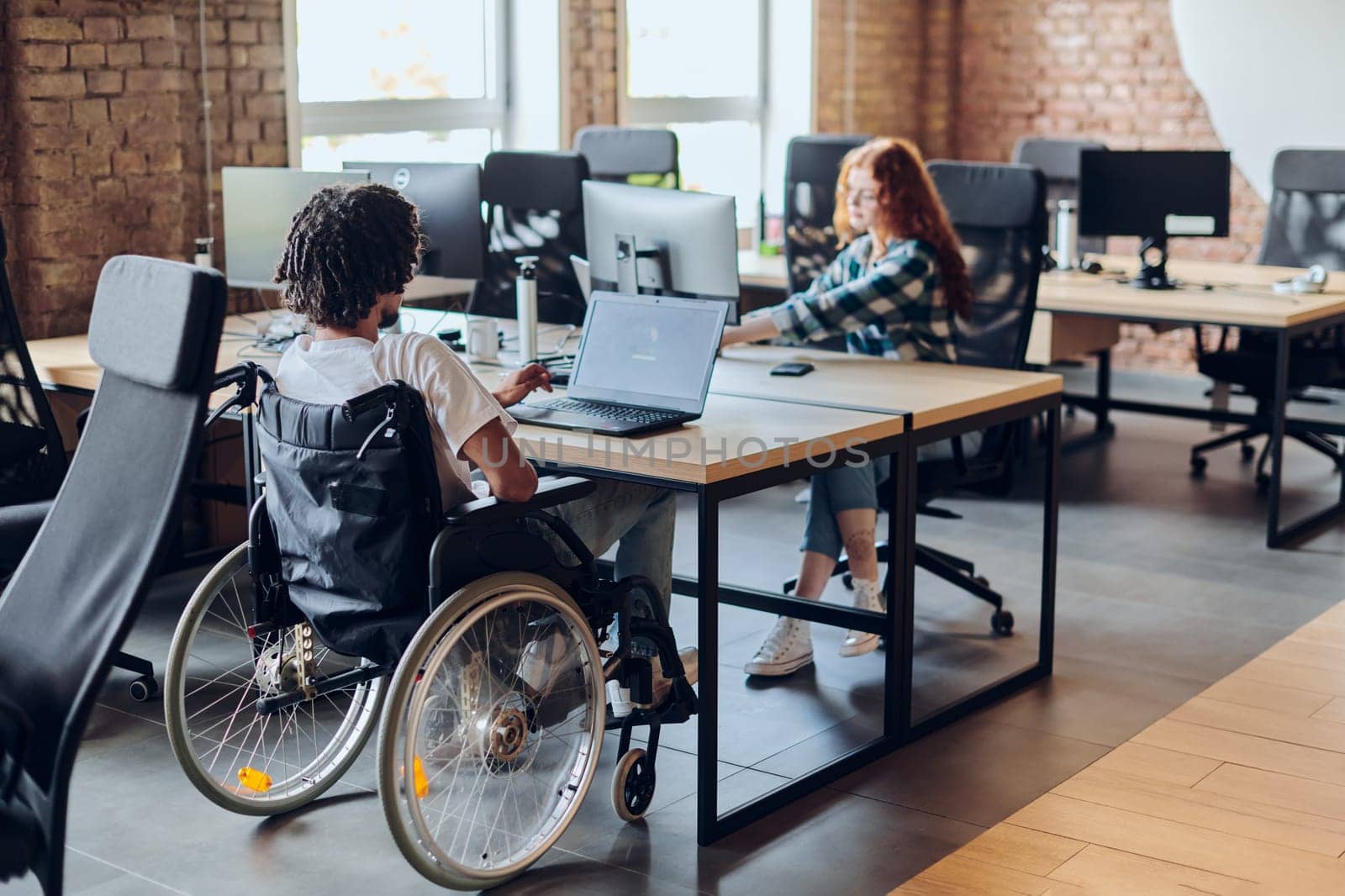 Business colleagues work within a modern startup coworking office, with one of them, an African America in a wheelchair, actively engaging with computers and laptops to collaboratively address various business challenges. by dotshock