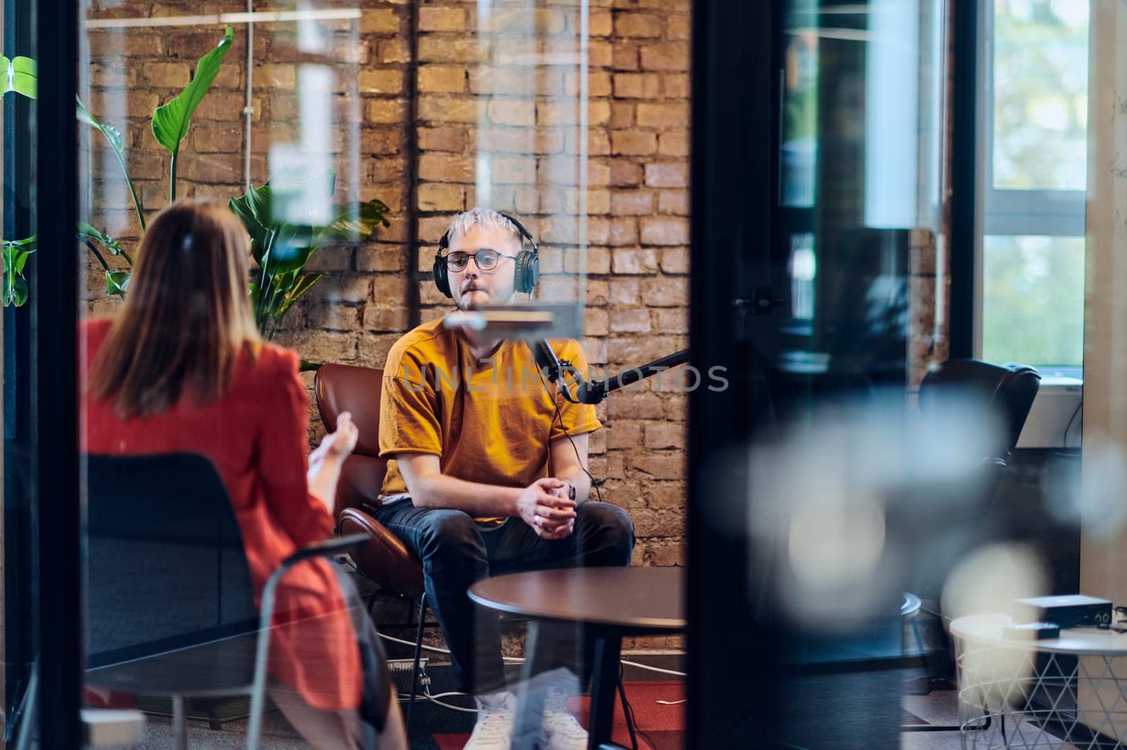 A gathering of young business professionals, some seated in a glass-walled office, engage in a lively conversation and record an online podcast, embodying modern collaboration and dynamic interaction by dotshock
