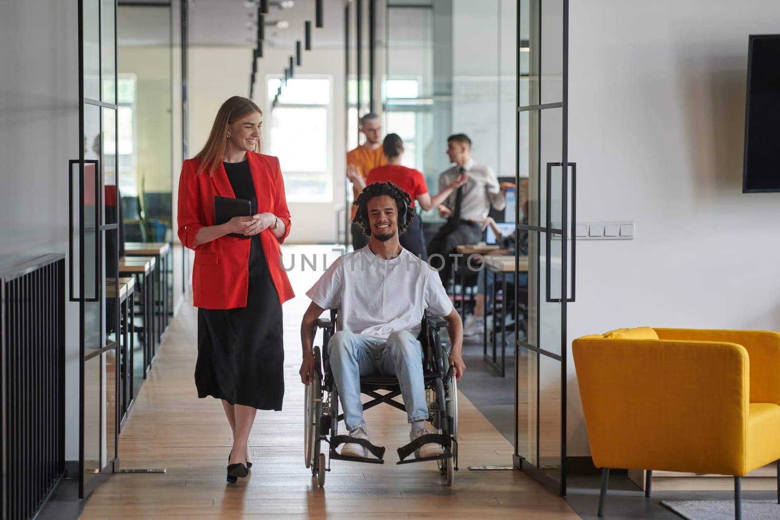 A group of young business people in a modern glass-walled office captures the essence of diversity and collaboration, while two colleagues, including an African American businessman in a wheelchair, reflect inclusivity and discuss solving business problems.