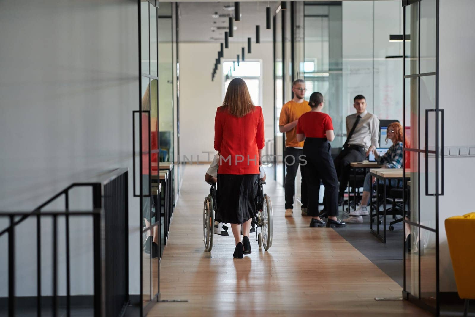 A group of young business people in a modern glass-walled office captures the essence of diversity and collaboration, while two colleagues, including an African American businessman in a wheelchair, reflect inclusivity and discuss solving business problems.