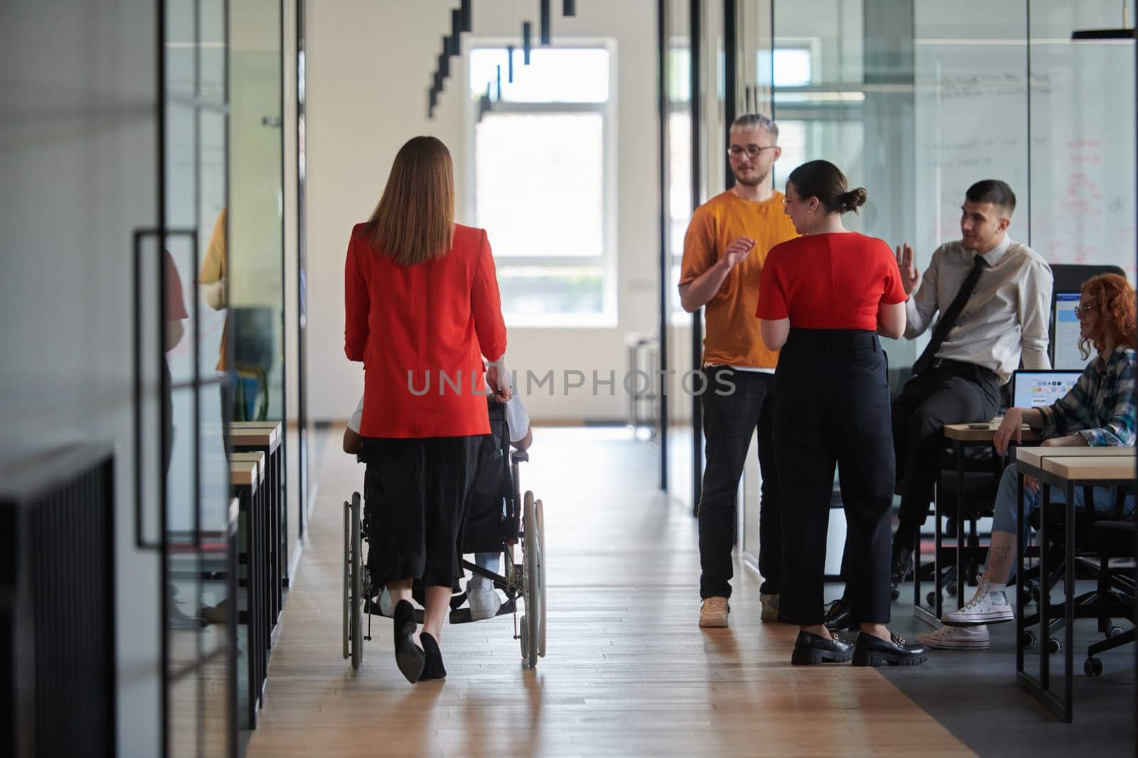 A group of young business people in a modern glass-walled office captures the essence of diversity and collaboration, while two colleagues, including an African American businessman in a wheelchair, reflect inclusivity and discuss solving business problems.