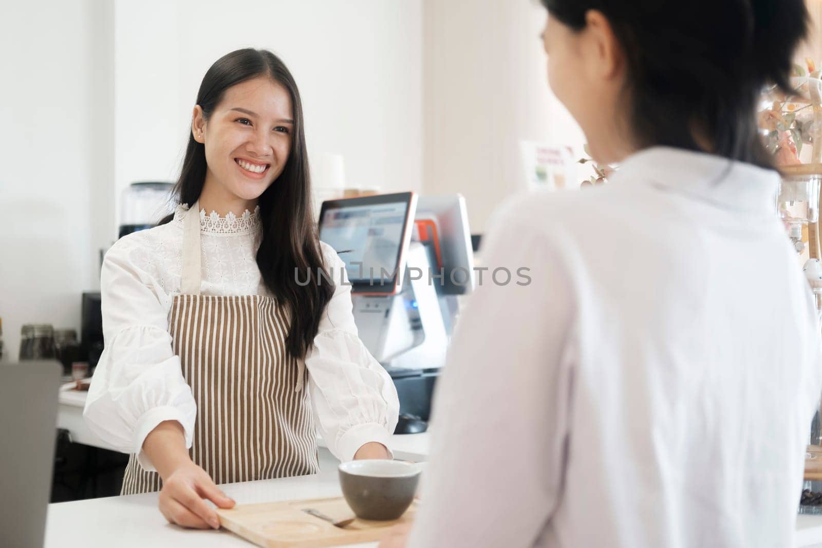 Coffee shop owner handing over a sealed coffee cup to a customer. Woman serving customer with a smile at a coffee shop. Smiling friendly barista serving a cup of coffe to customer at coffee shop. Coffee small business concept.