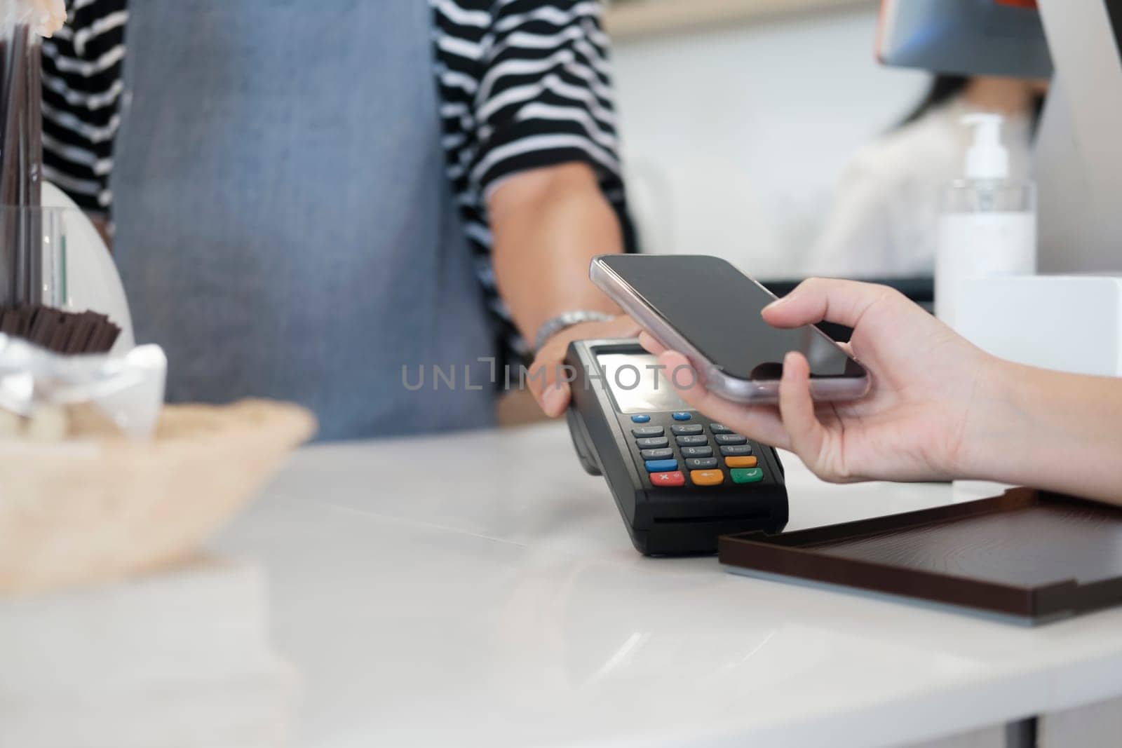 Female customer holding phone near nfc terminal make contactless mobile payment with waitress barista saleswoman on coffeeshop counter, woman client pay in cafe with cellphone via pos machine. Tap-to-pay technology is so convenient.