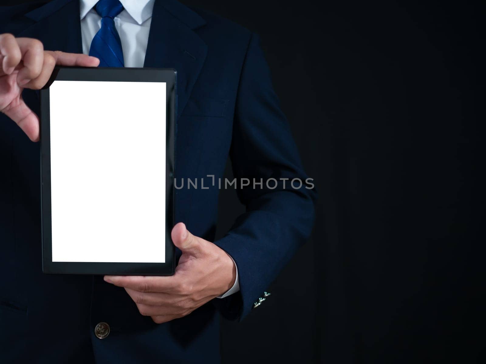 Businessman standing holding white screen tablet on dark background. Advertising concept. Banner sign.