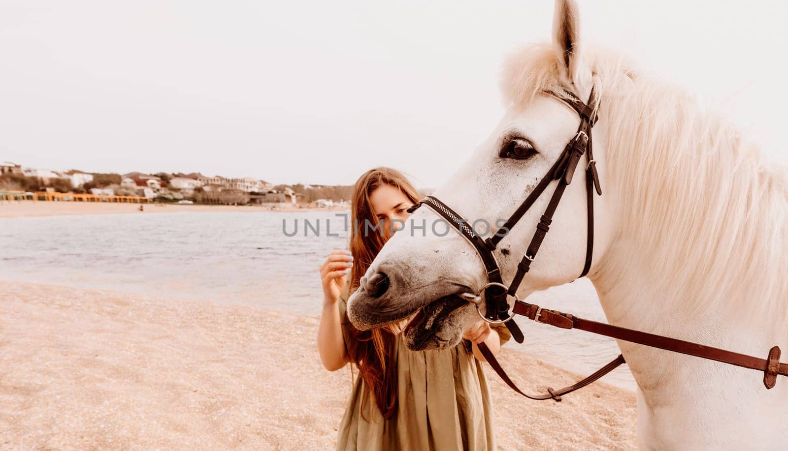 A white horse and a woman in a dress stand on a beach, with the sky and sea creating a picturesque backdrop for the scene