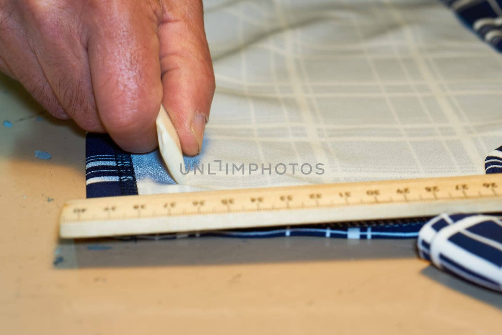 The tailor's hand measures the distance on the fabric with chalk and a ruler by jovani68