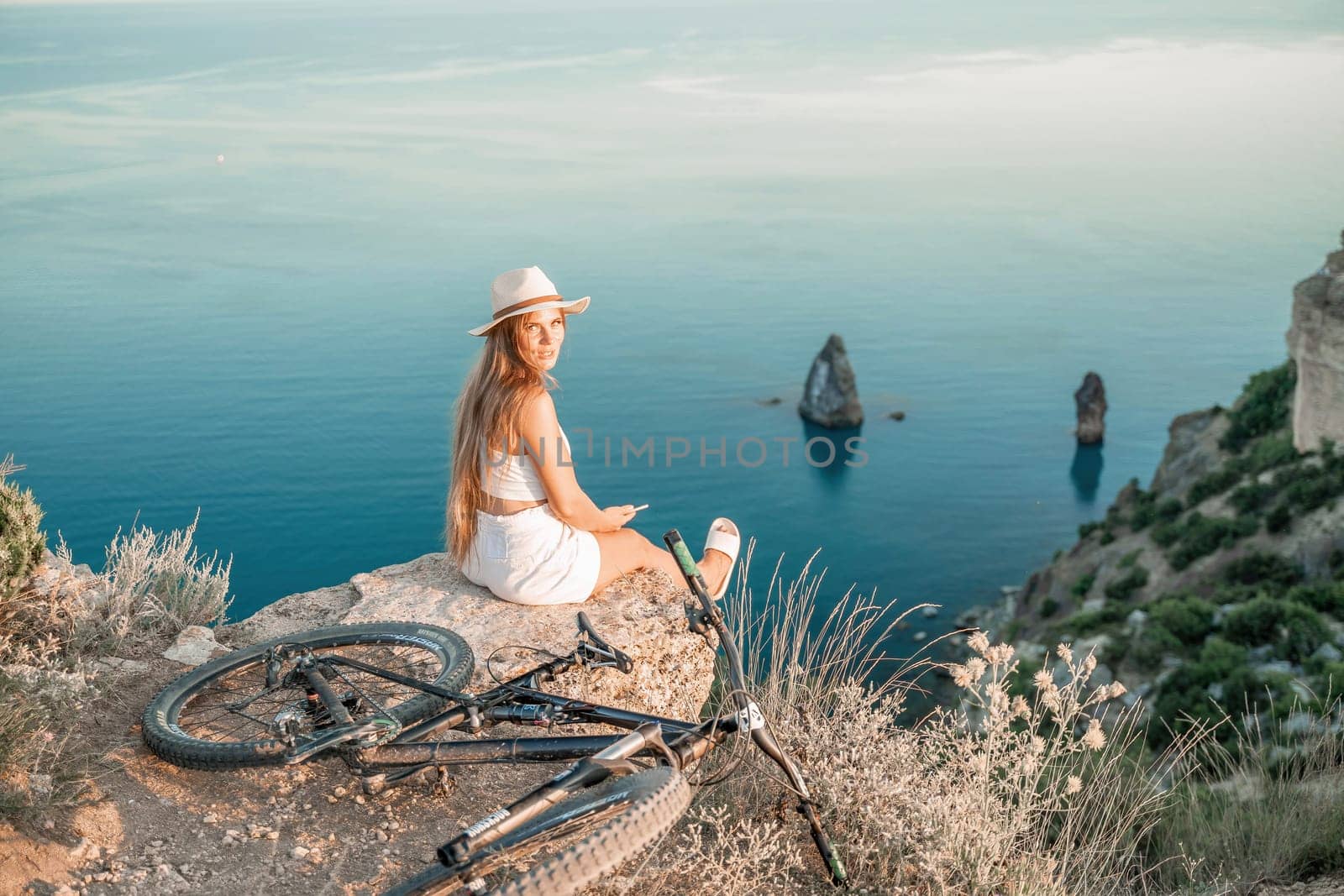 A woman cyclist on a mountain bike looking at the landscape of mountains and sea. Adventure travel on bike