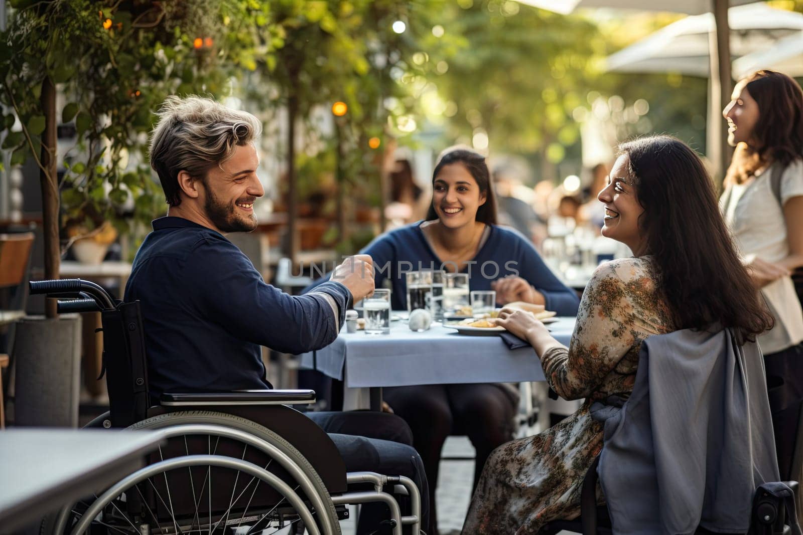 Disability man in wheelchair sitting at table enjoying breakfast with his friends and spending time together by papatonic