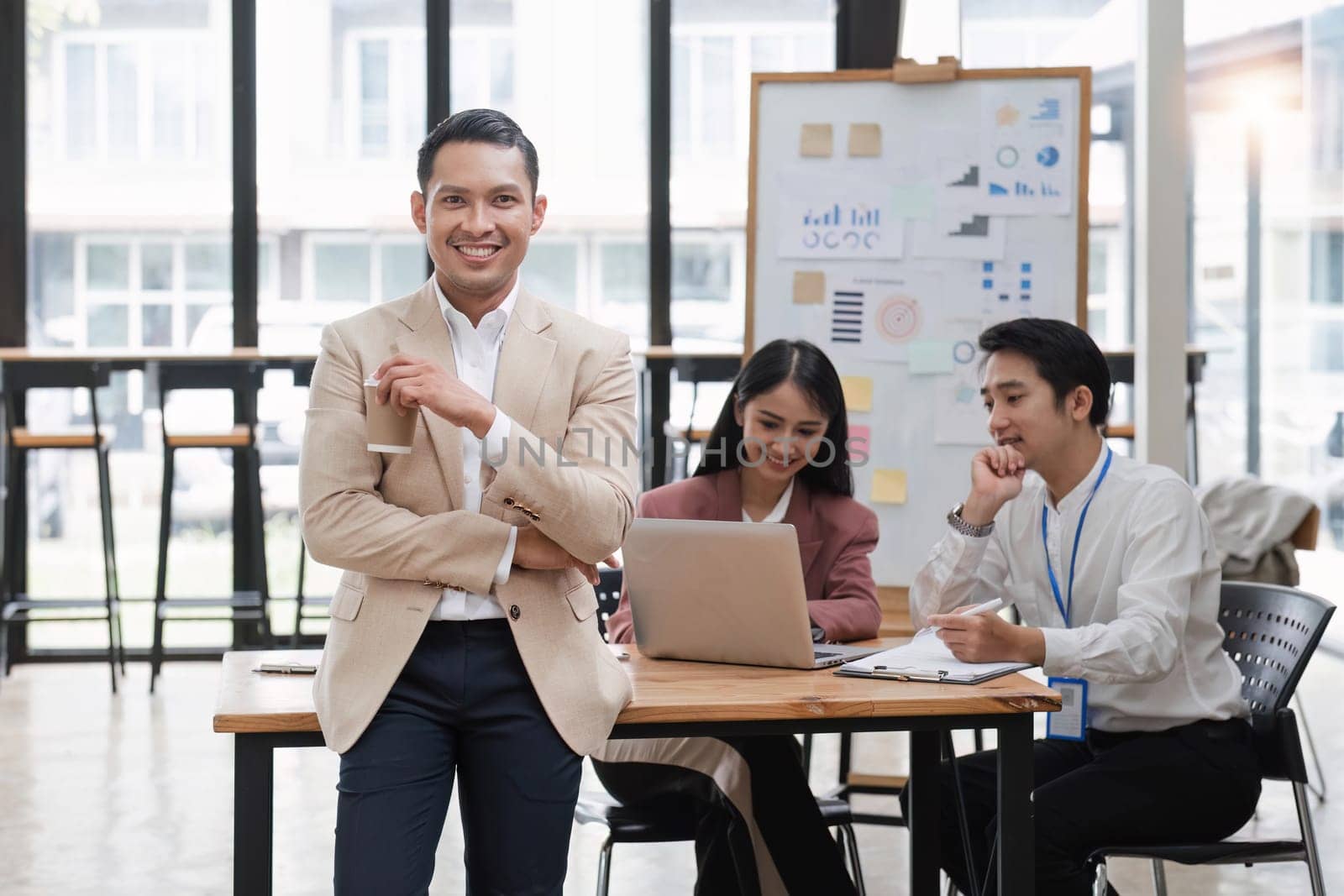 Portrait of a young businessman standing in an office where employees are working..