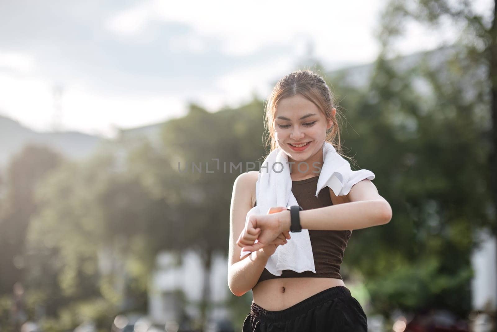 Young woman jogging and looking at his smart watch in the evening at the park. by wichayada