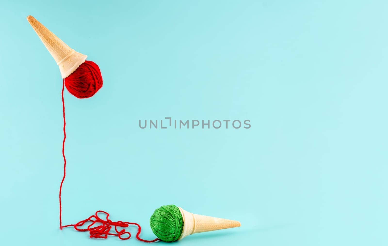 two waffle cones with red and green yarn instead of ice cream hobby concept on blue background by Iryna_Melnyk