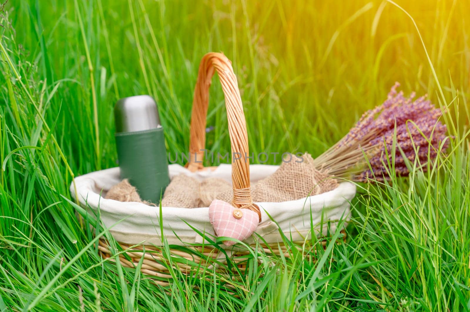 basket with a bouquet of lavender thermos and  heart  in the grass for a picnic