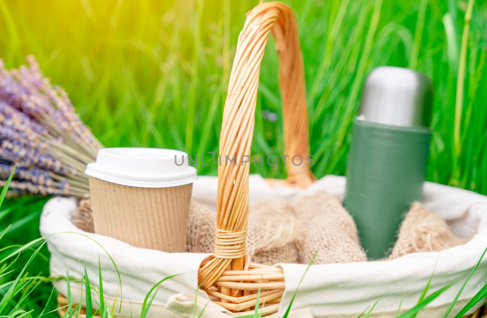 basket with a bouquet of lavender thermos and a craft cup of coffee in the grass for a picnic