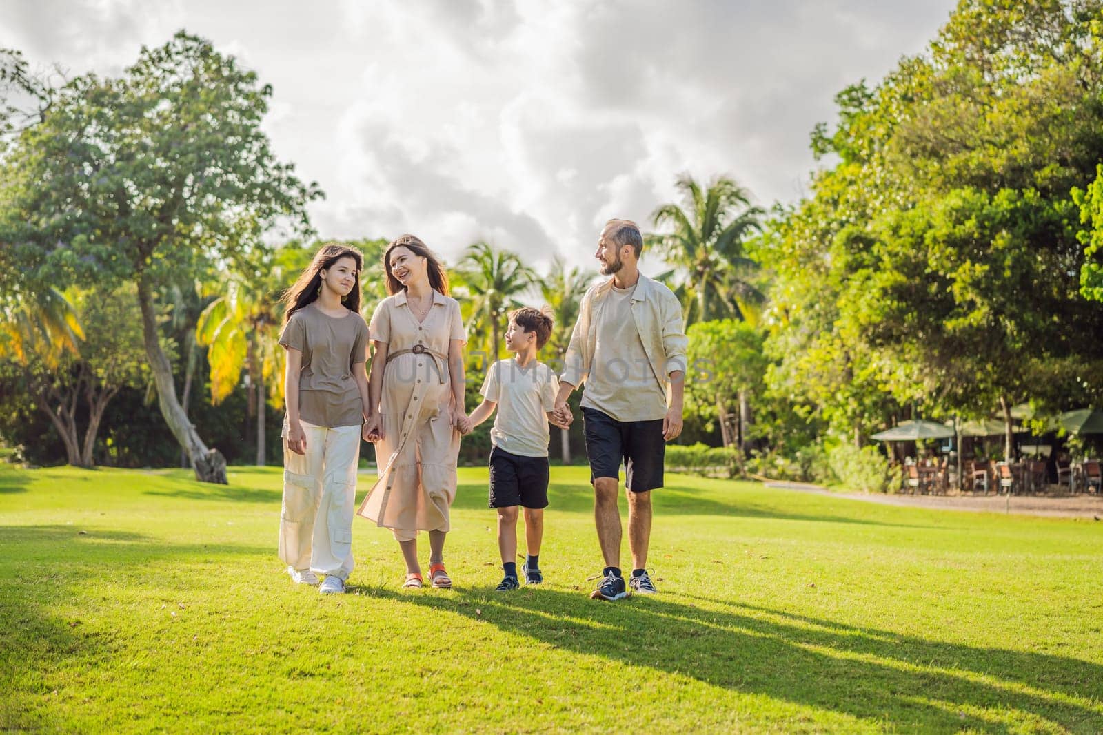 A loving family enjoying a leisurely walk in the park - a radiant pregnant woman after 40, embraced by her husband, and accompanied by their adult teenage children, savoring precious moments together amidst nature's beauty. Pregnancy after 40 concept.