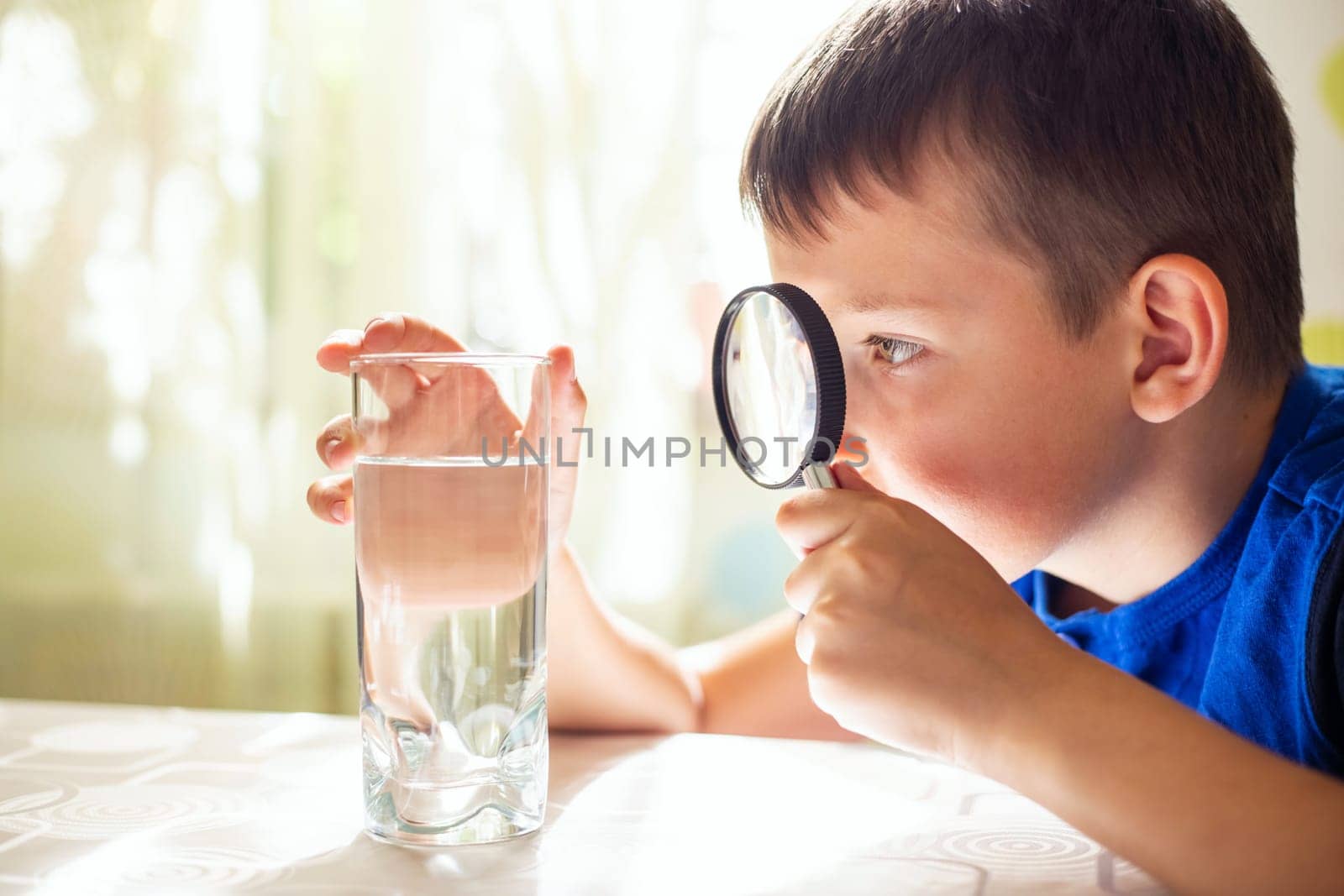 The child boy looking at water in a glass through magnifying glass. Water quality check concept.