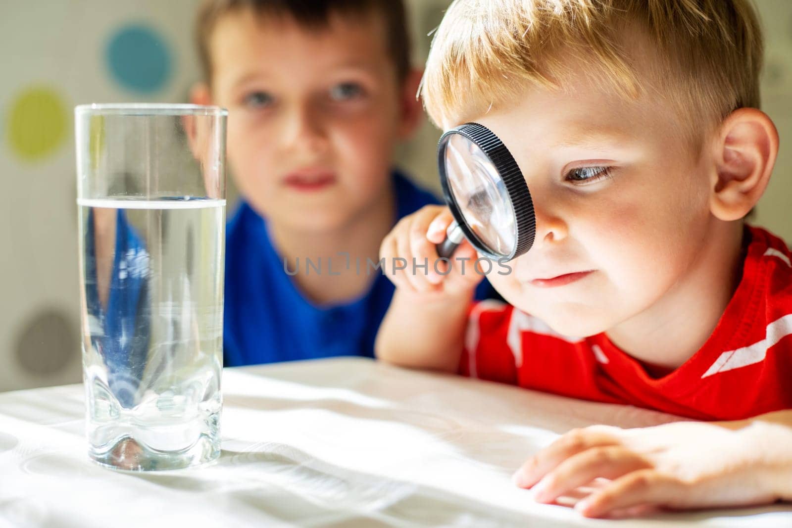 The child boy looking at water in a glass through magnifying glass by andreyz