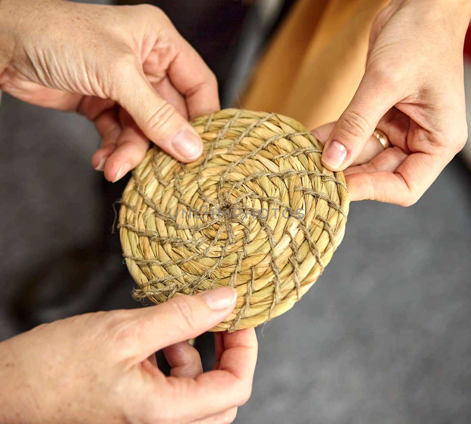 Basket sewing master grass weaver. Three hands hold a round grass mat.