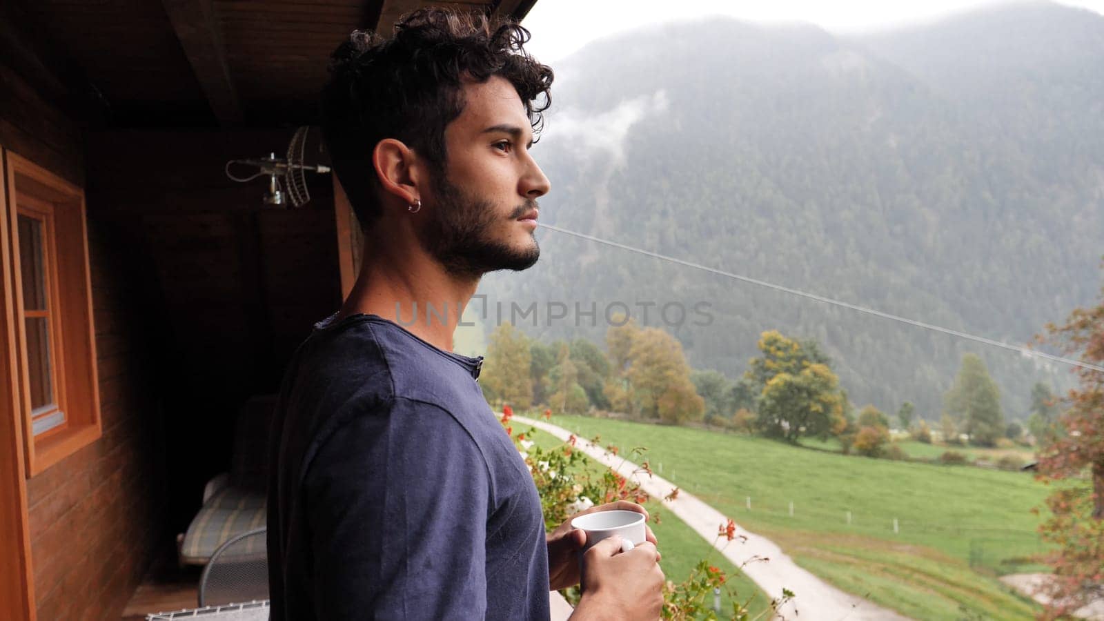 A man standing on a porch with a cup of coffee. Young man enjoying a morning cup of coffee on a balcony in the moutains