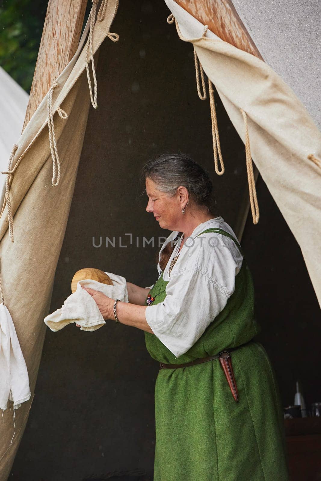 Hojbjerg, Denmark, July 29, 2023: The hostess rubs the plate in the tent in rain at the Viking Festival.
