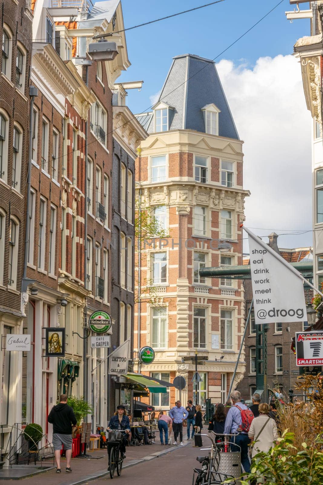 Netherlands. Sunny summer day in the center of Amsterdam. Facades of typical Dutch houses with various advertising signs and flags and people on a narrow pedestrian street