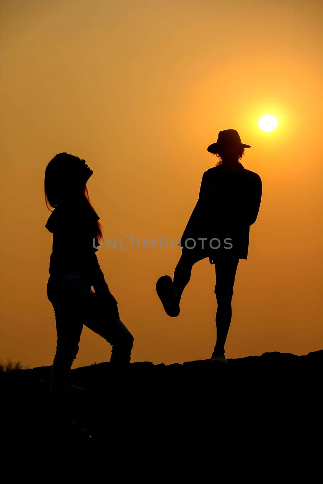 Women and men silhouettes on a rock at sunset.