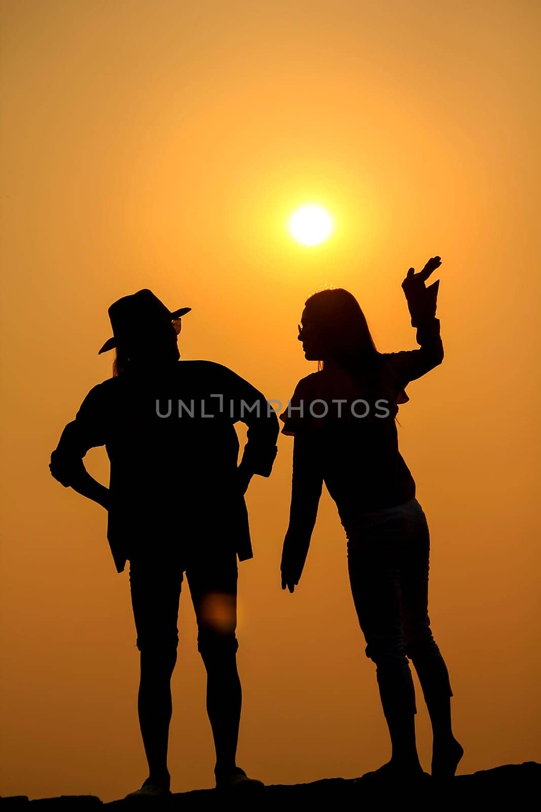 Women and men silhouettes on a rock at sunset.