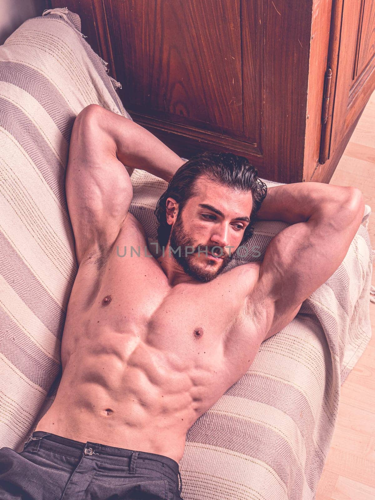 Handsome shirtless muscular young man at home laying on couch, an expression of tranquility, in a health and fitness concept