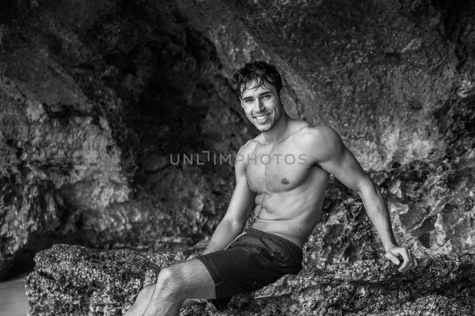 Half body shot of a handsome young man standing on a beach in Phuket Island, Thailand, shirtless wearing boxer shorts, showing muscular fit body, looking at camera