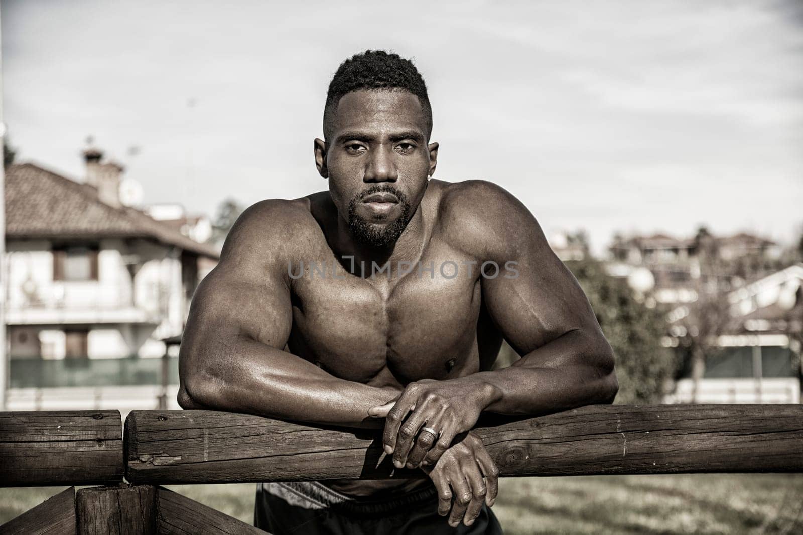 A shirtless african american man leaning on a wooden fence