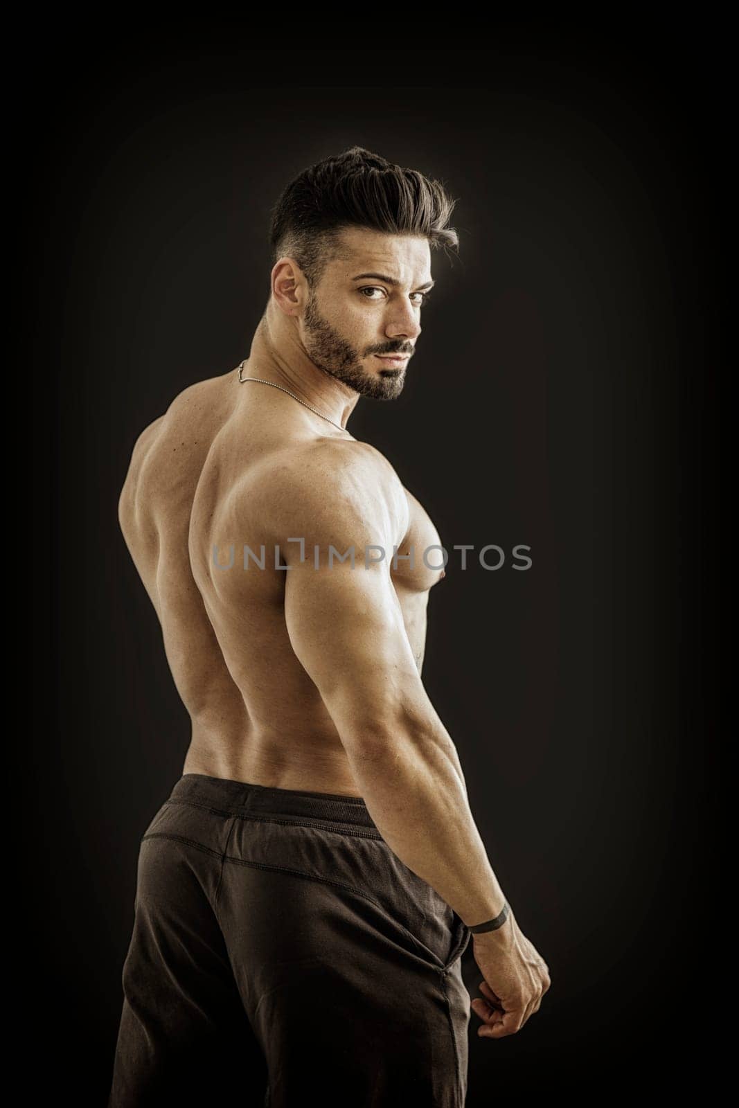 A shirtless man with no shirt posing for a picture, against black background in studio